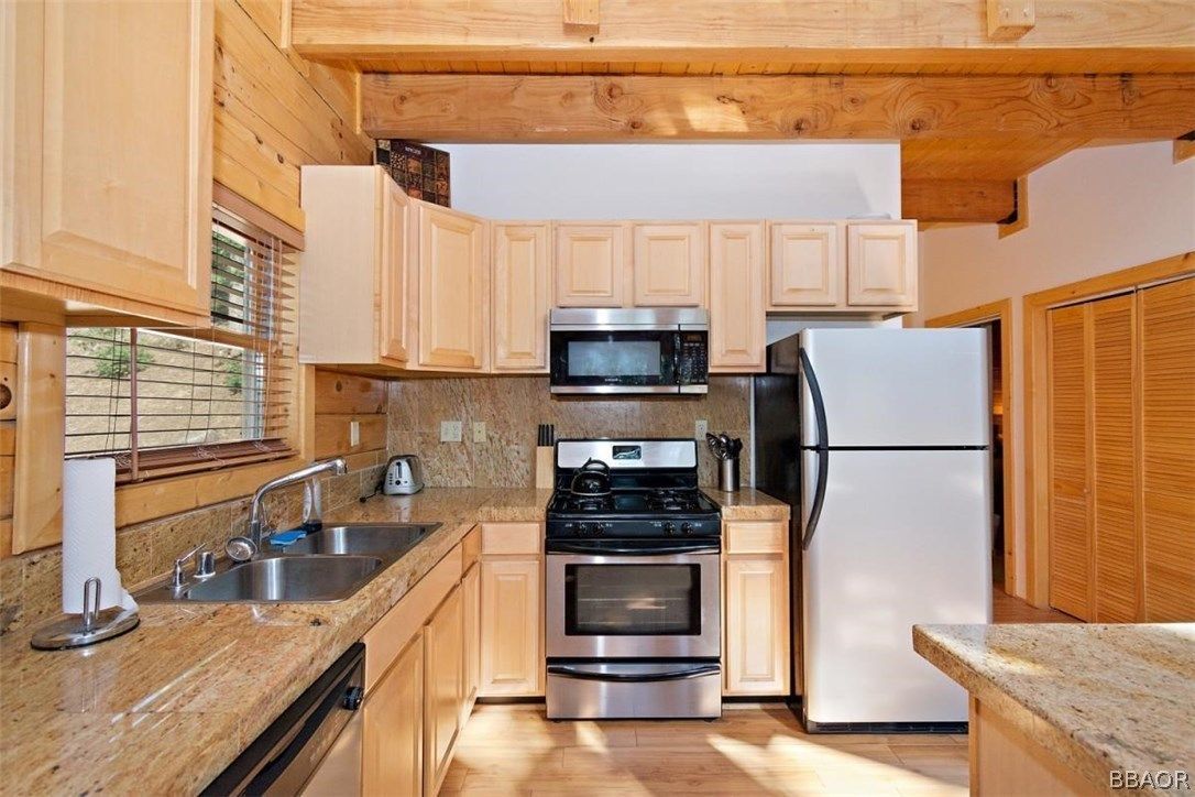 Kitchen with light wood cabinets, granite countertops, stainless steel appliances, and a window.