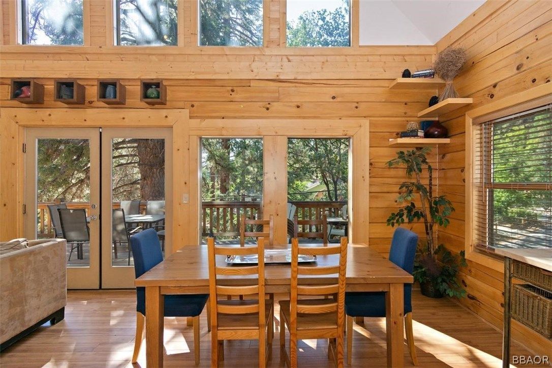 Dining area with a wooden table, chairs, and large windows overlooking a deck and trees.