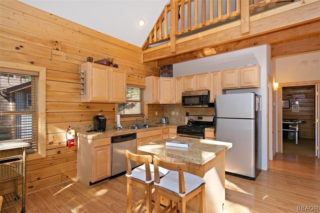 Kitchen in a cabin with light wood walls, cabinets, and island, a microwave and refrigerator, and a small window.