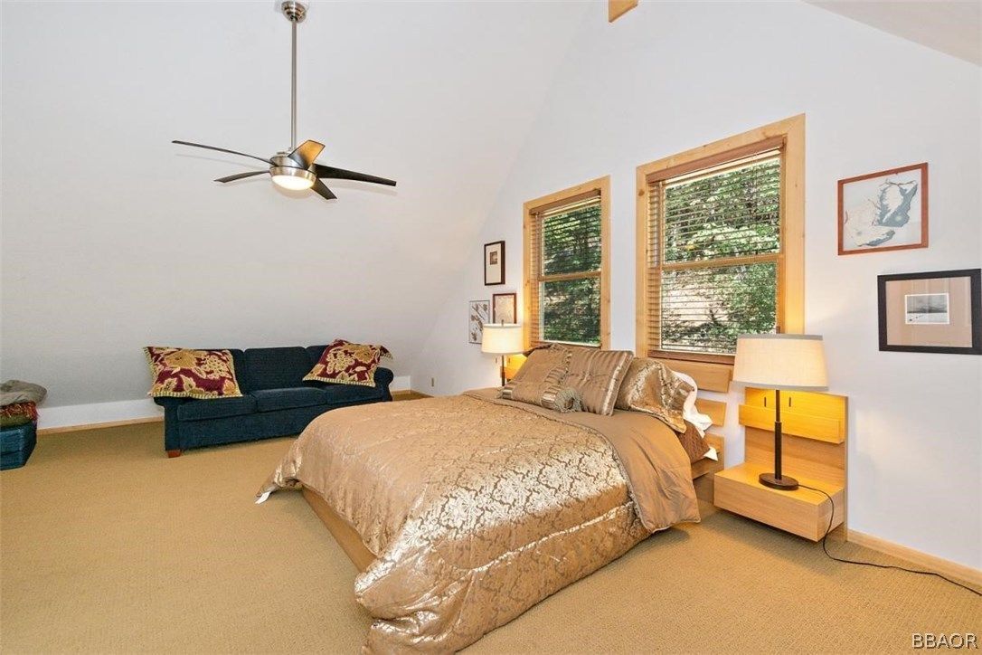 Bedroom with bed, couch, two windows, and light-colored carpet and walls.