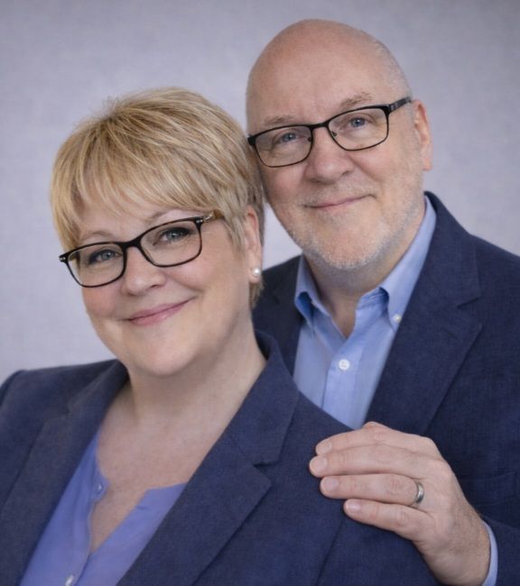 A man and a woman are posing for a picture in front of a bookshelf