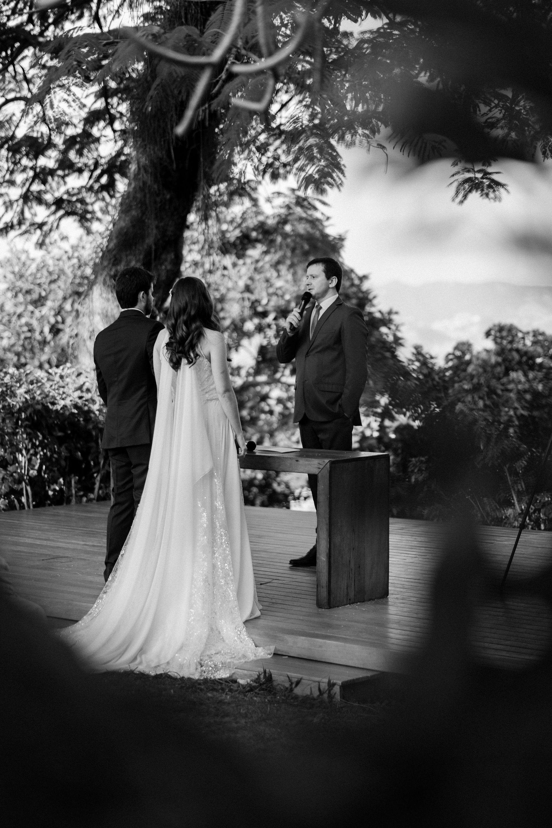 A black and white photo of a bride and groom standing under a tree.
