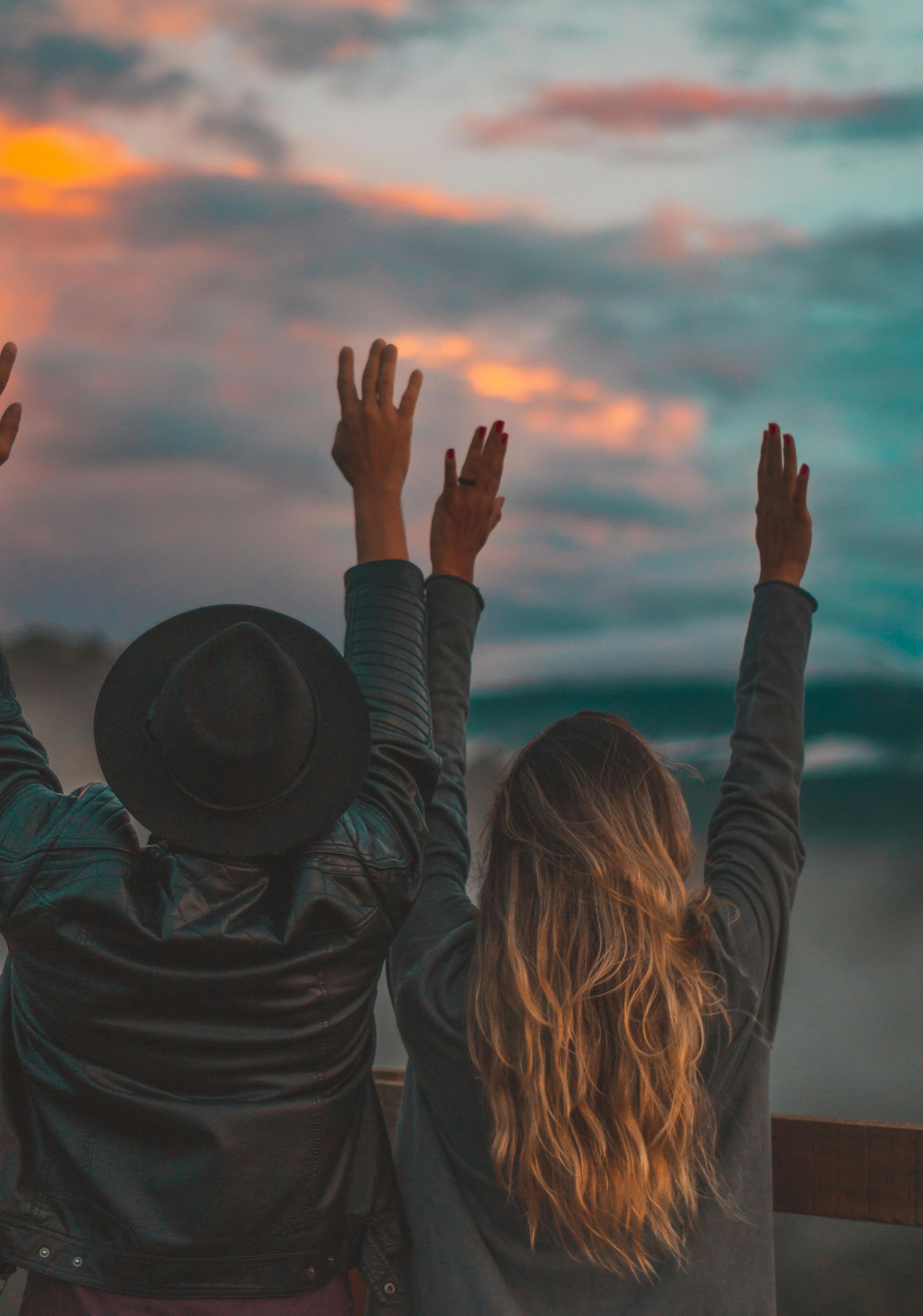 Two women are sitting on a bench with their arms in the air.