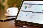 Tablet displaying data charts with a pie chart and line graph, cup of coffee, and phone on desk.