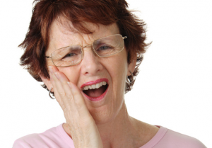 Woman with glasses holding her cheek and grimacing in pain on a white background