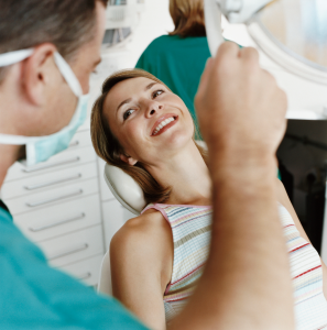 Dentist examining a smiling patient in a dental chair with a handheld mirror
