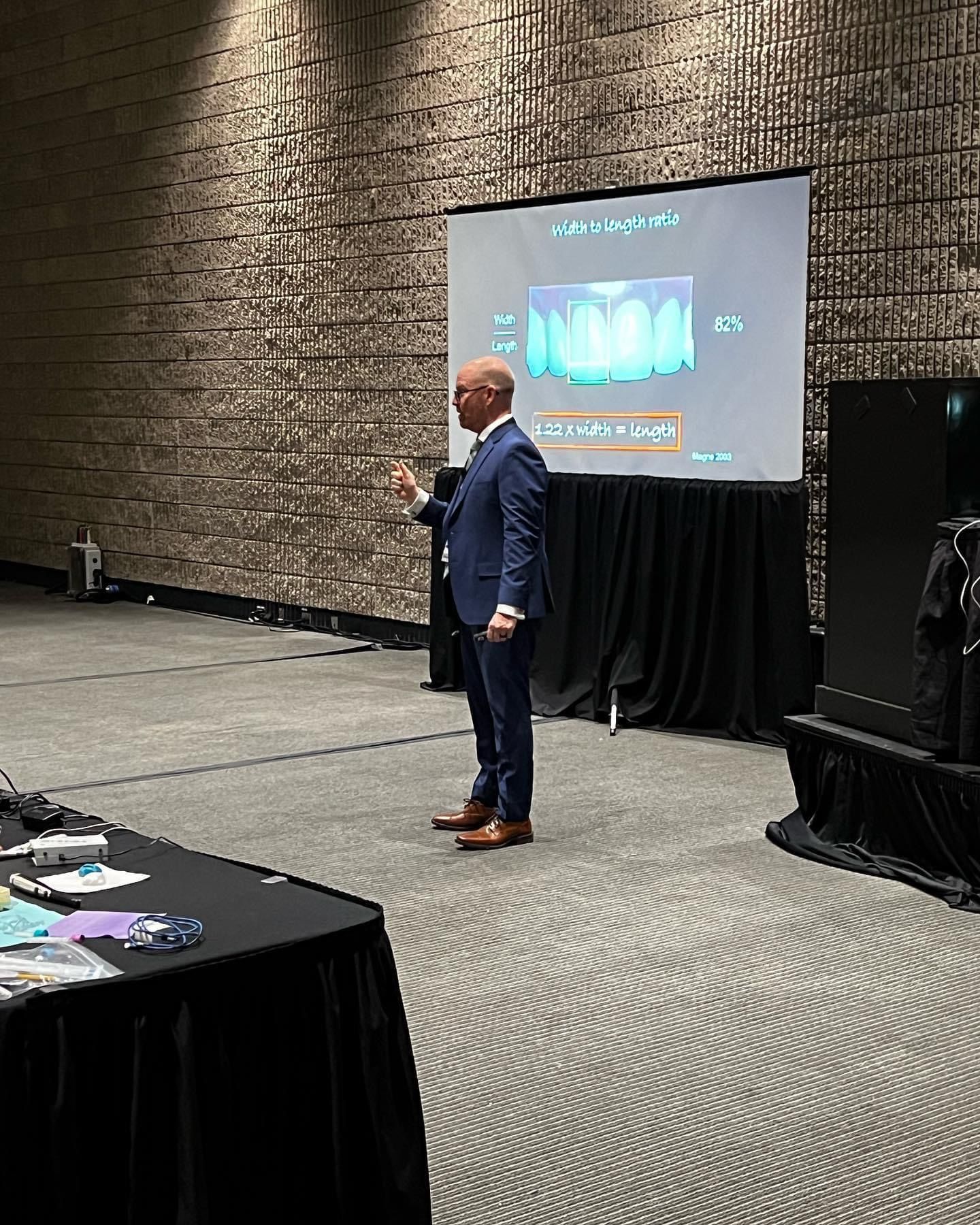 Speaker presenting on stage beside a projected slide in a conference room