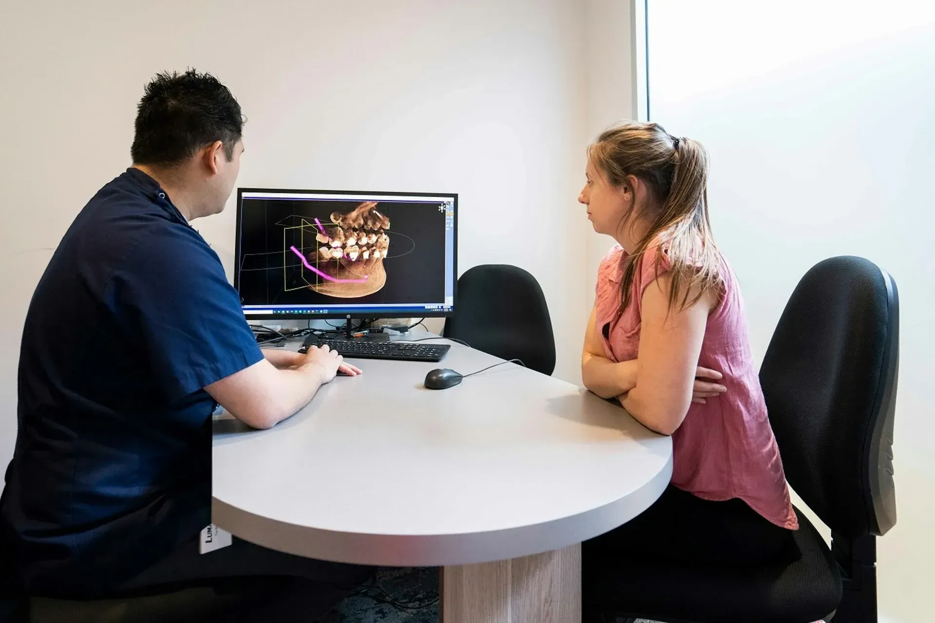 Two people discuss a dental scan on a computer in a clinic office