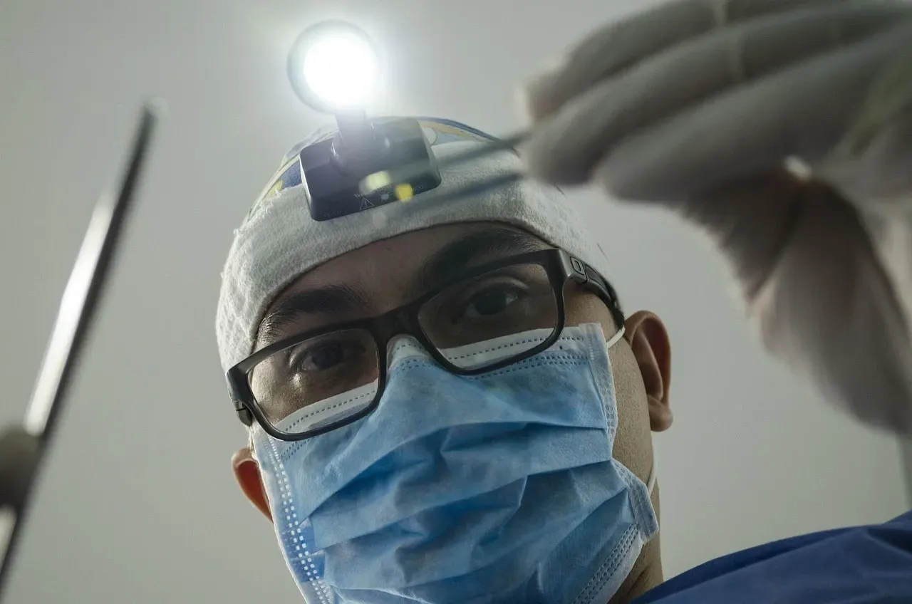 Dentist in mask and gloves holding a dental tool under a bright exam light