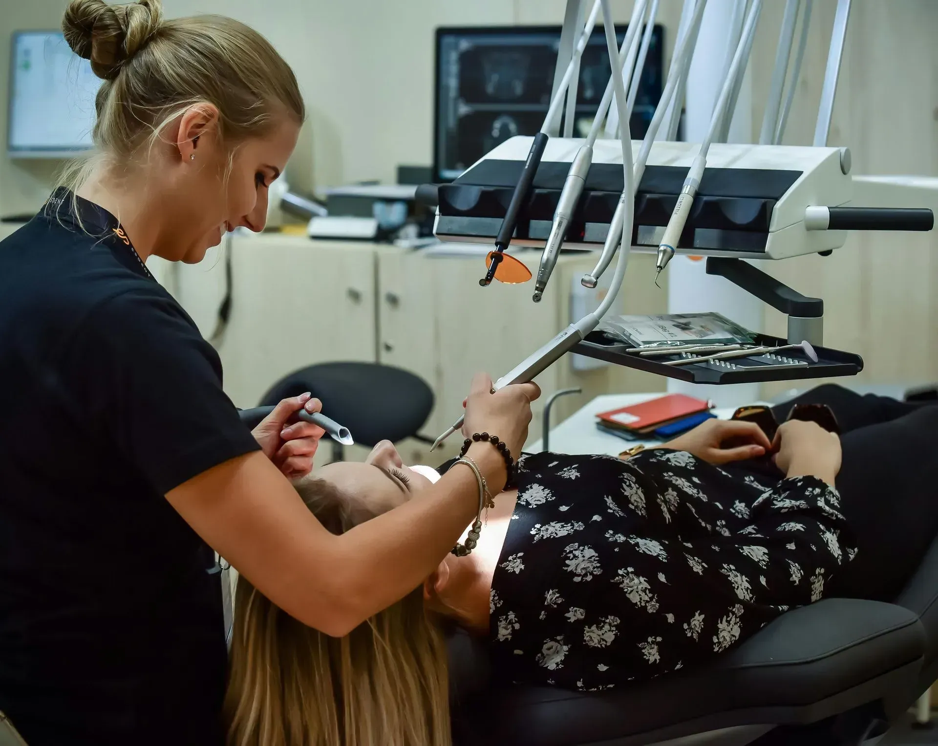 Dentist examining a patient in a reclining chair with dental tools overhead