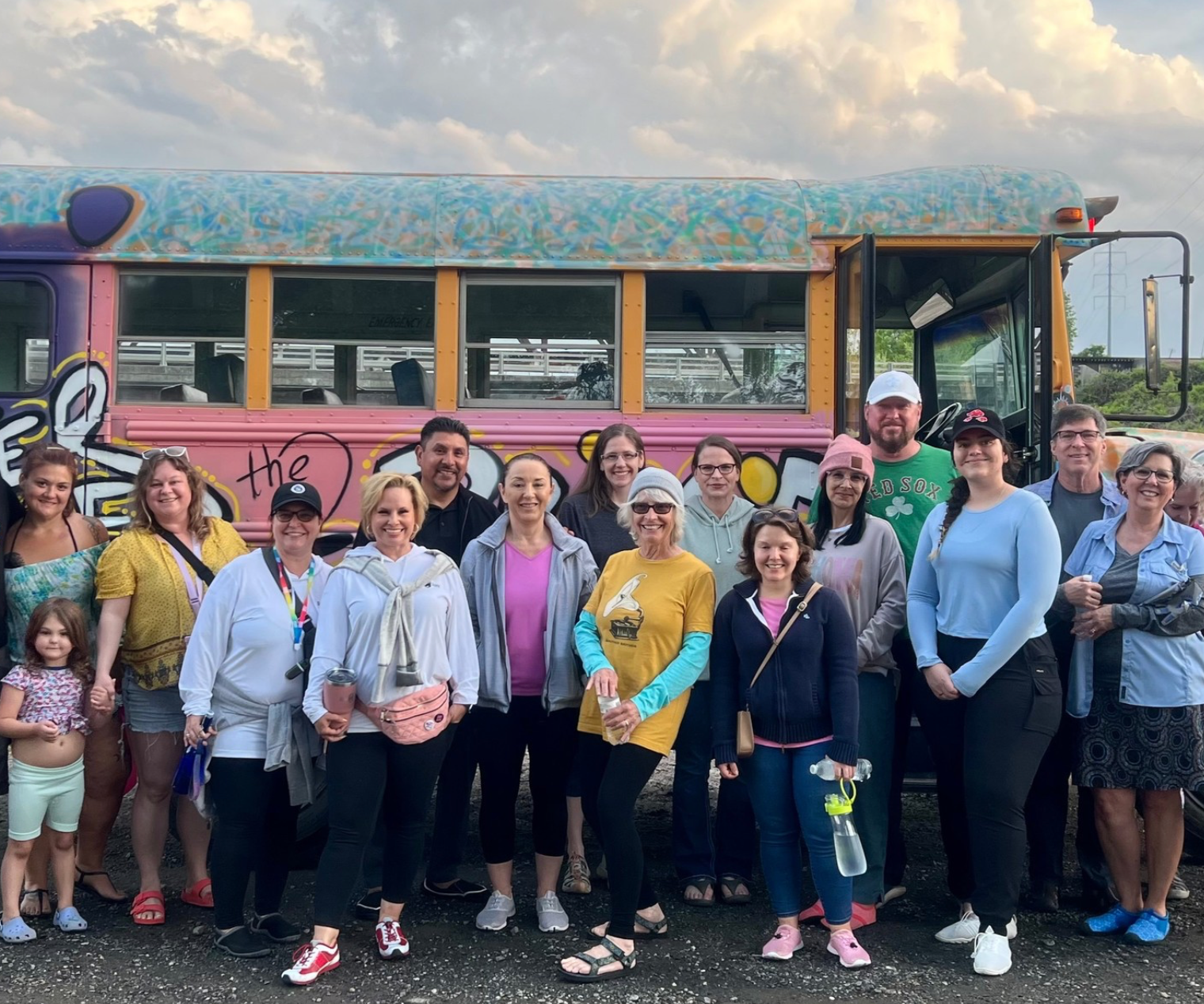 Group of people pose in front of a colorful bus with graffiti, in an outdoor setting.