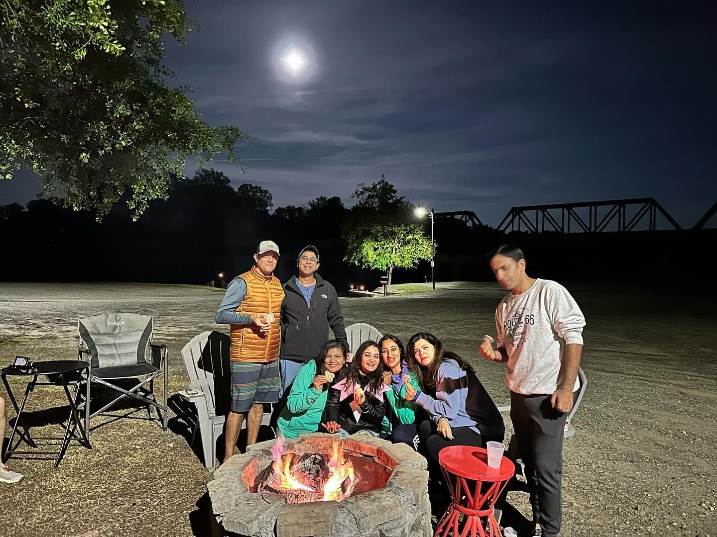 People gathered around a campfire at night; full moon overhead.