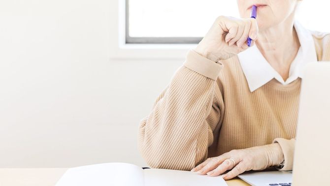 an older woman sitting at a desk with a pen in her mouth