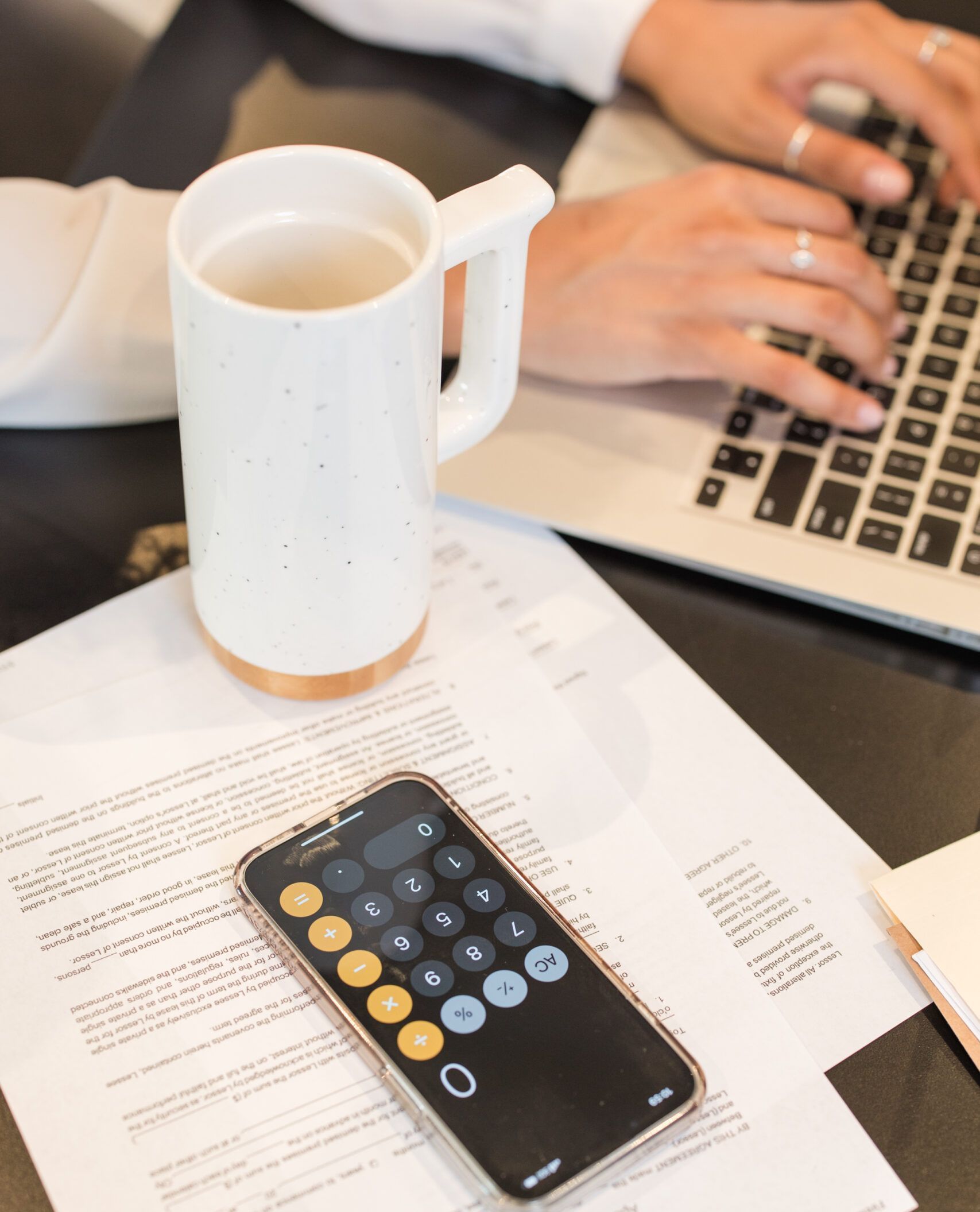 a person is typing on a laptop next to a cup of coffee and a calculator