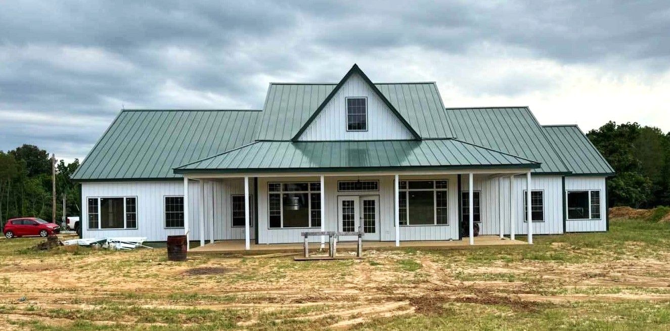 Stockade Living building of a White farmhouse with green metal roof under cloudy sky.