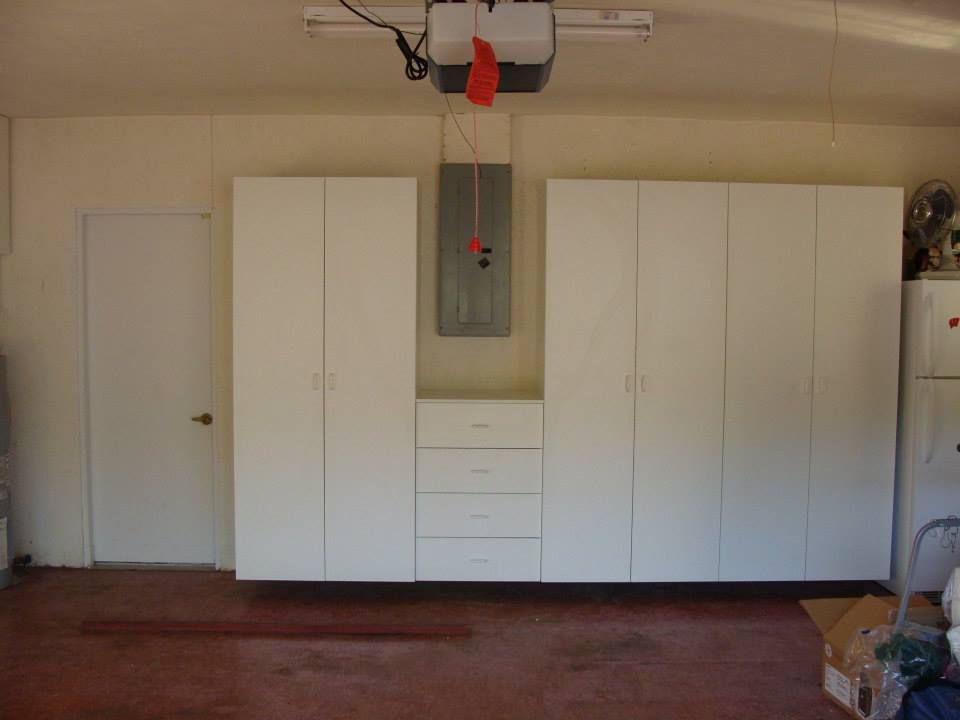 A garage with lots of white cabinets and drawers