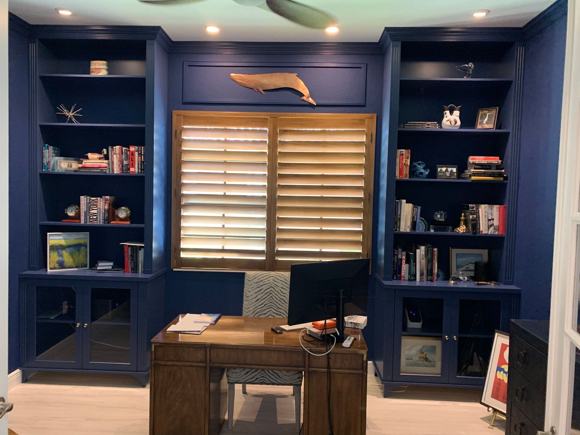 A home office with a desk , shelves , and a ceiling fan.