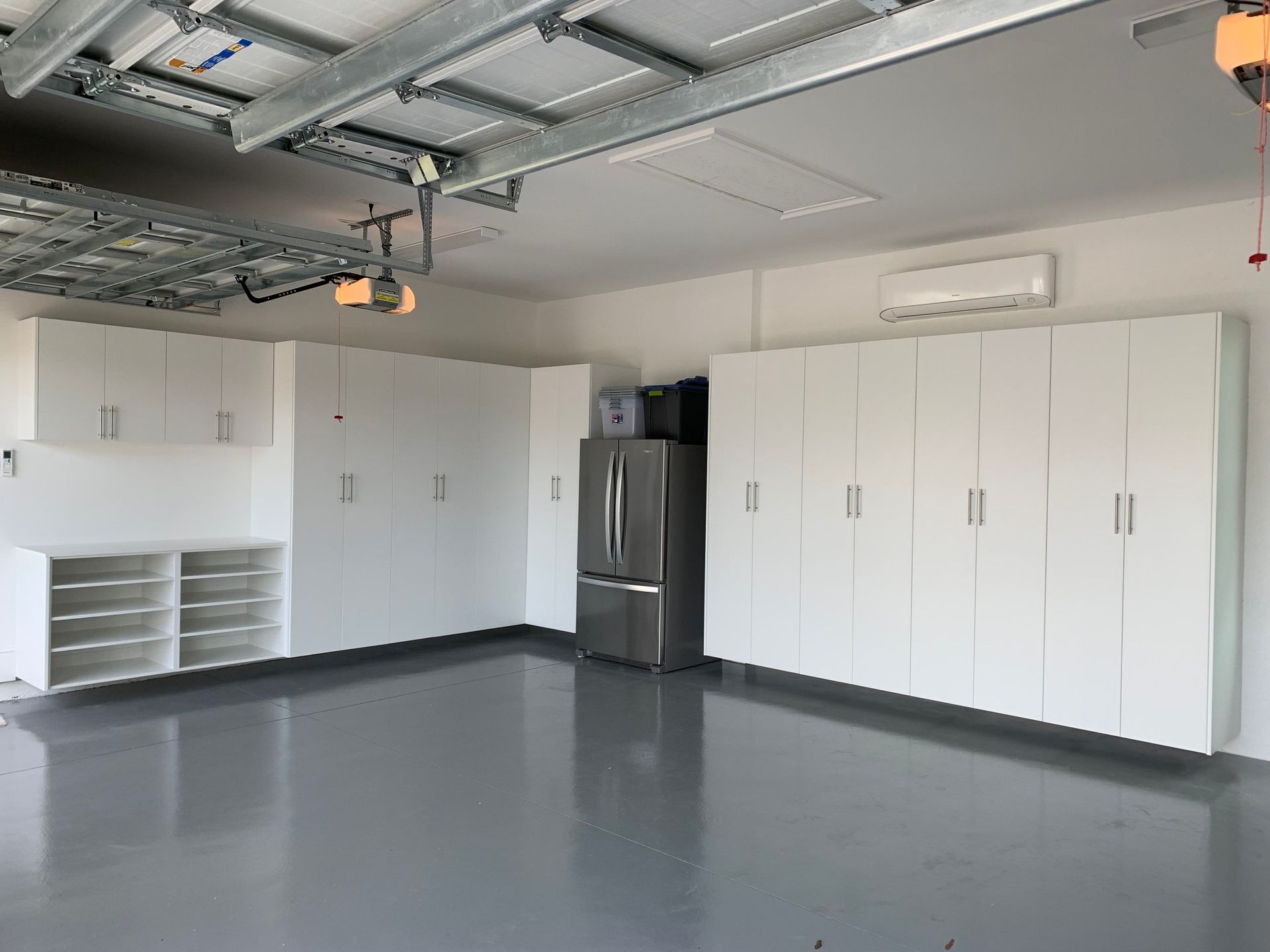 A large empty garage with white cabinets and a refrigerator.