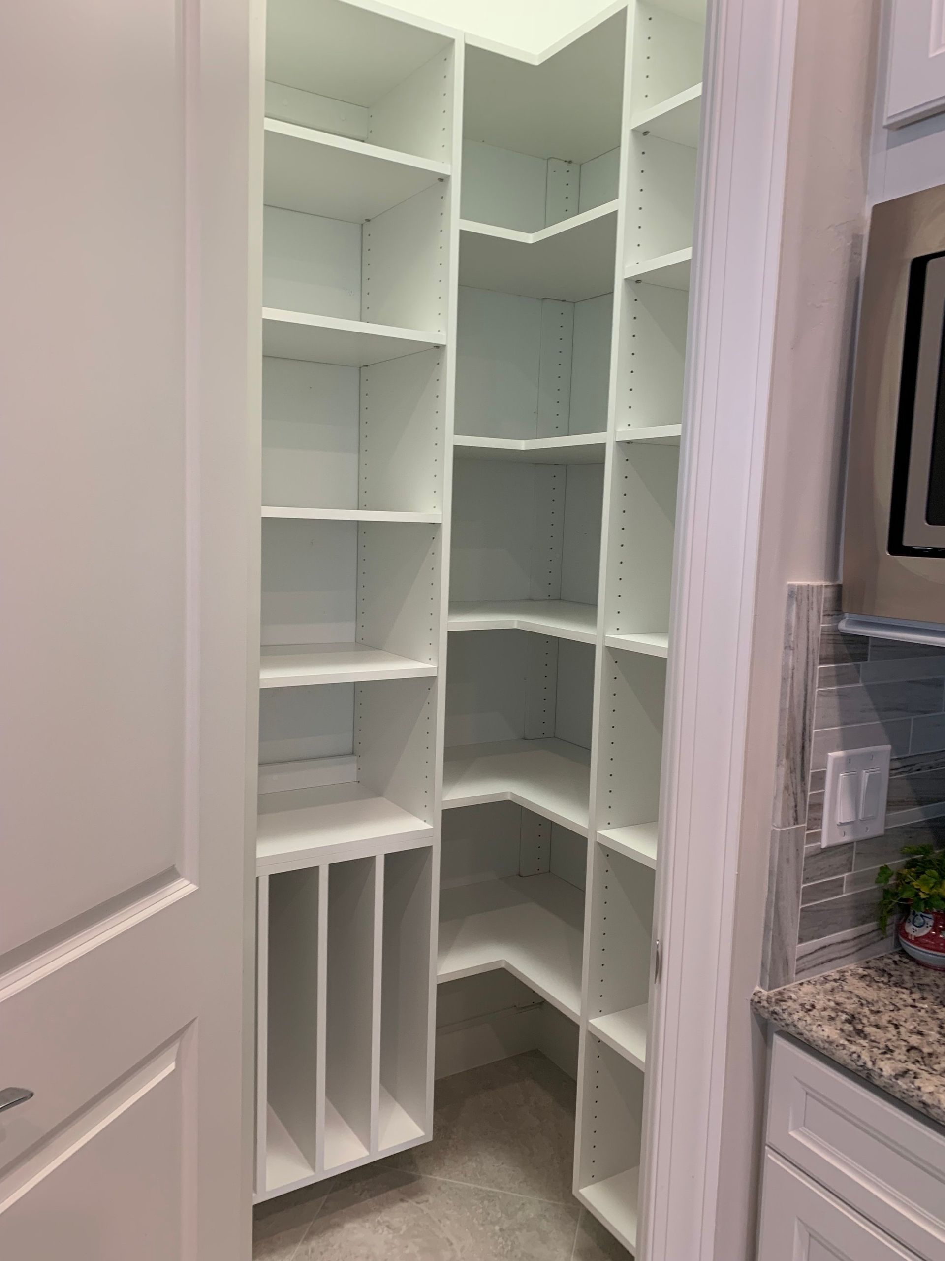 A pantry with lots of shelves and a microwave in a kitchen.
