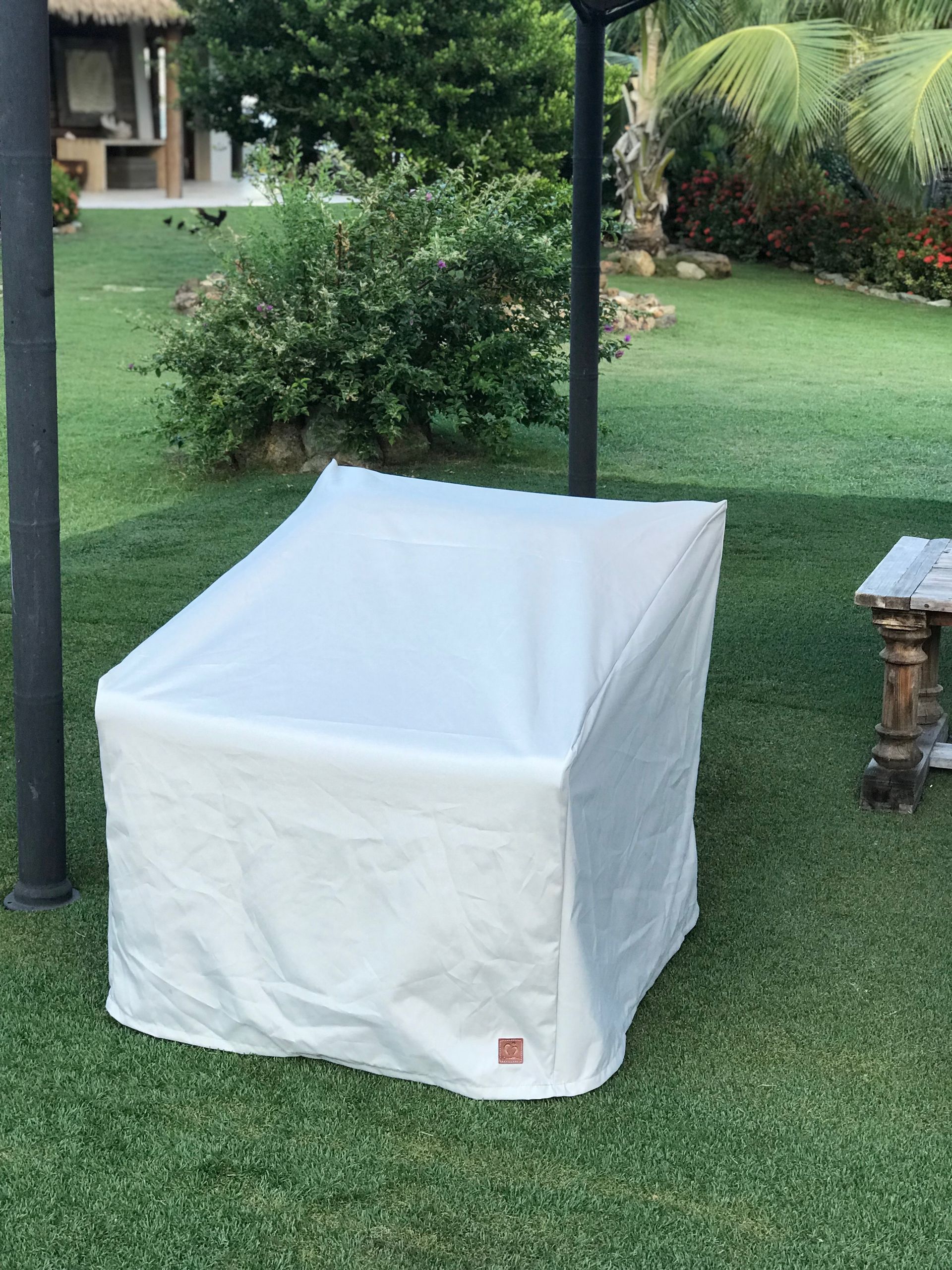 A white chair covered with a protective cover sits on a green lawn in a yard. 