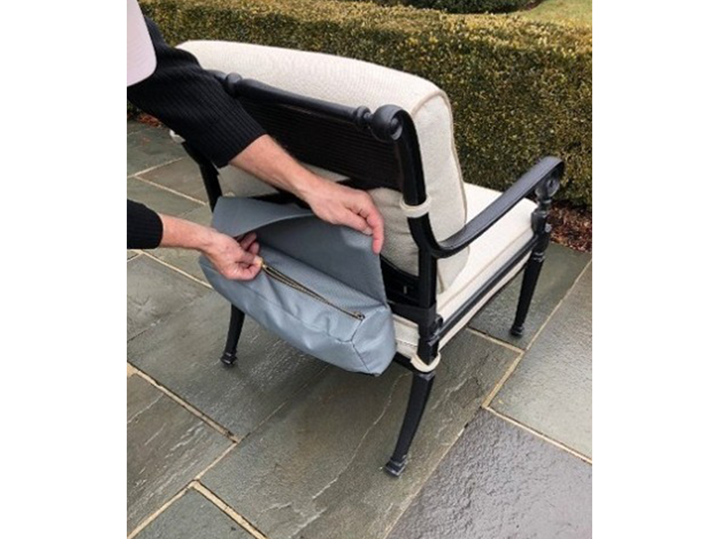 Person zipping up a gray bag attached to the back of a black and white outdoor armchair on a stone patio.