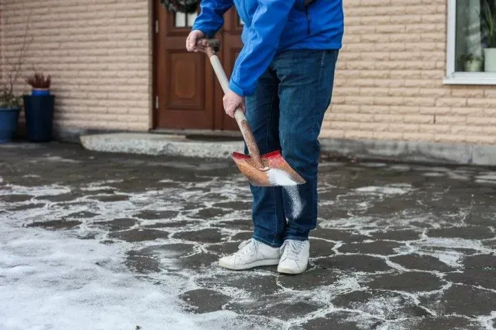 Person spreading ice melt salt on a cleared stone patio.