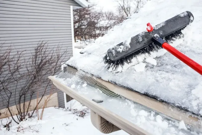 Using a roof rake to remove heavy snow and ice from house gutters.