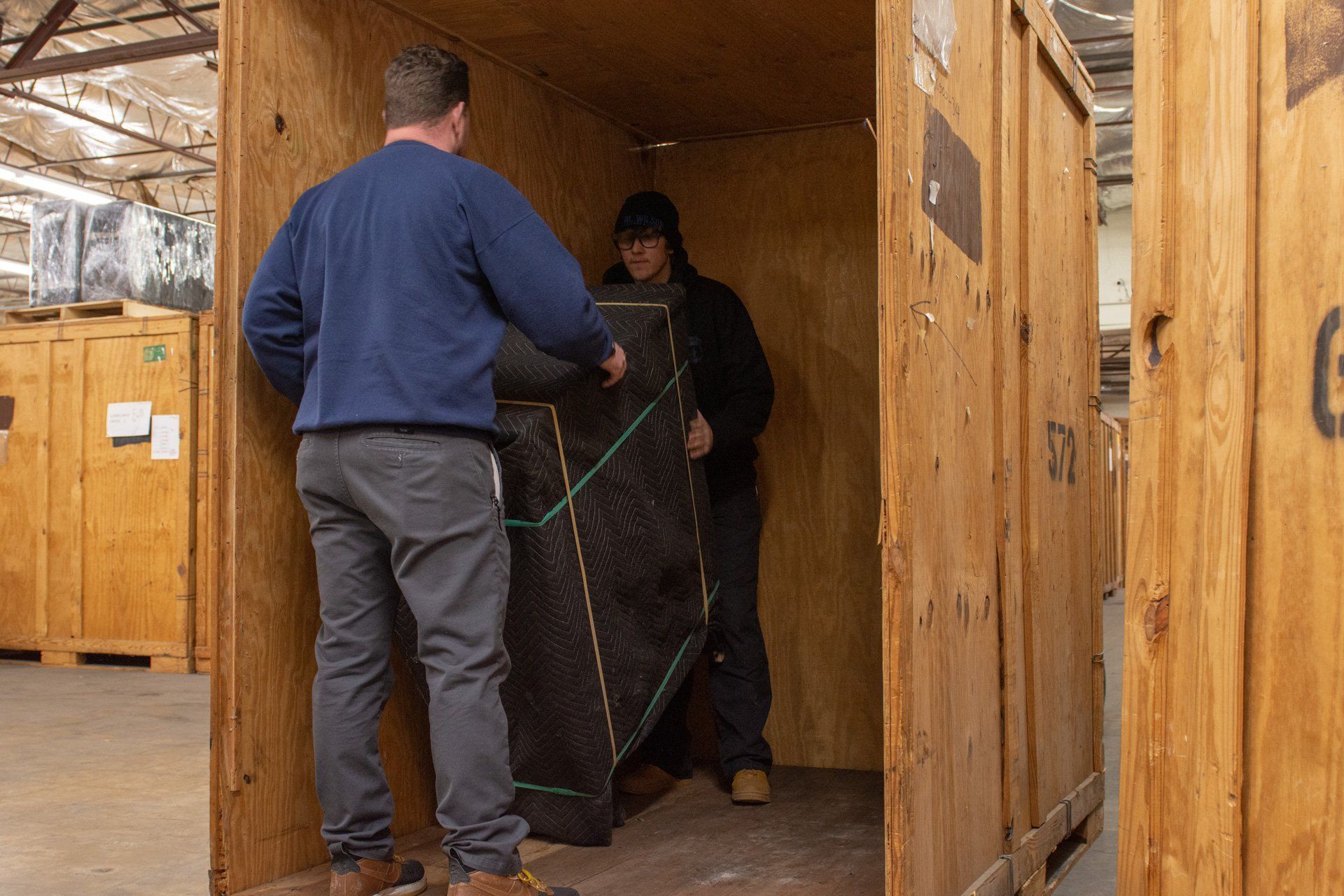 Two men are moving a large piece of furniture into a wooden crate.