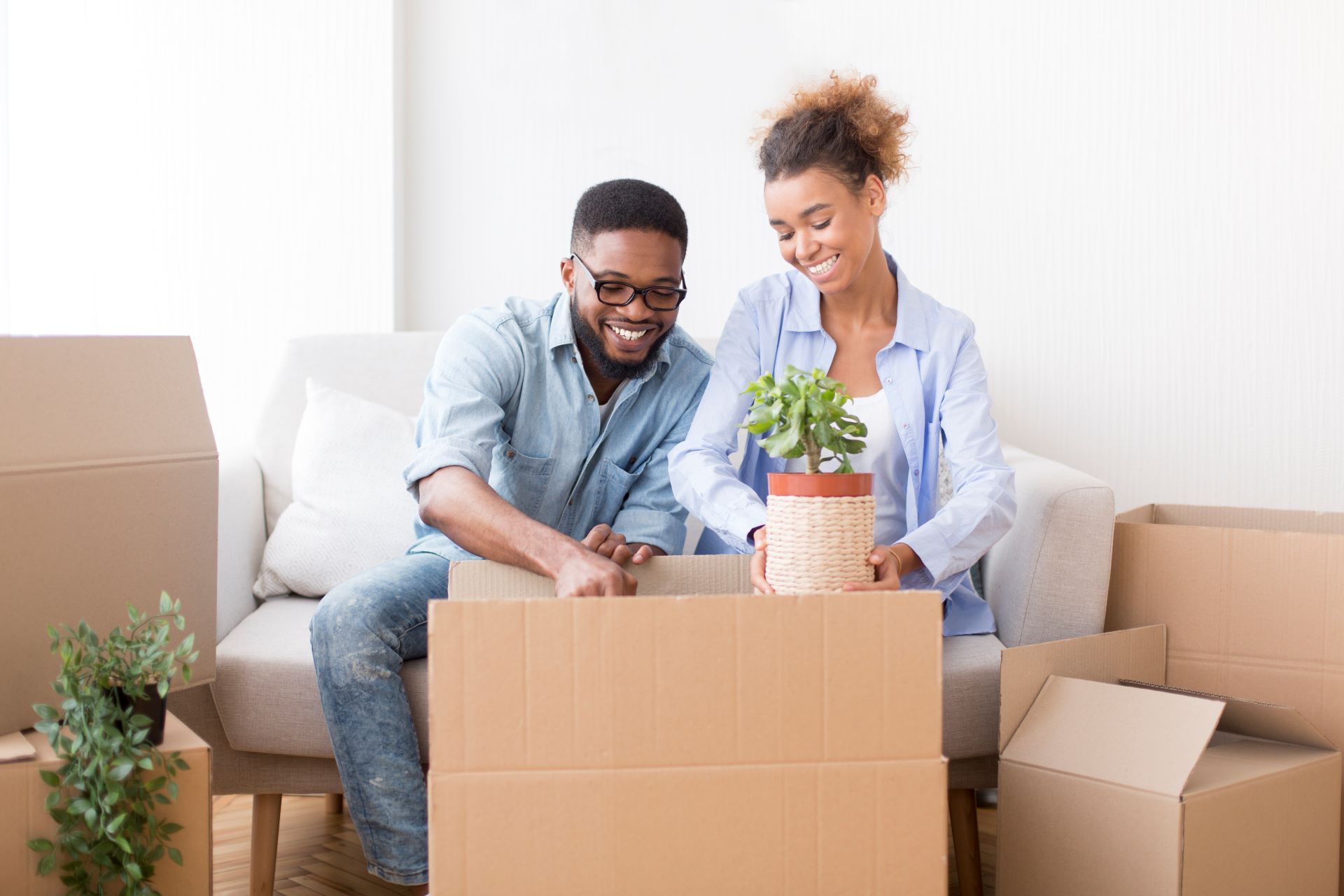 A man and a woman are sitting on a couch looking at a potted plant in a cardboard box.