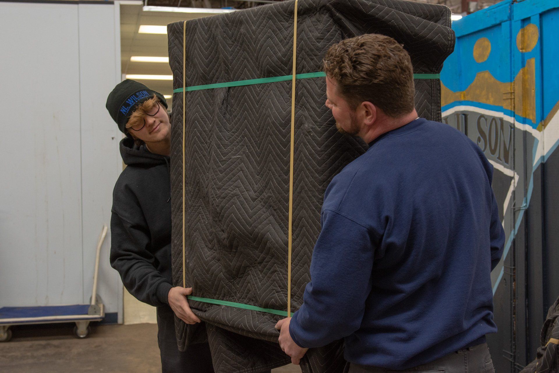 Two men are carrying a large piece of furniture in a warehouse.