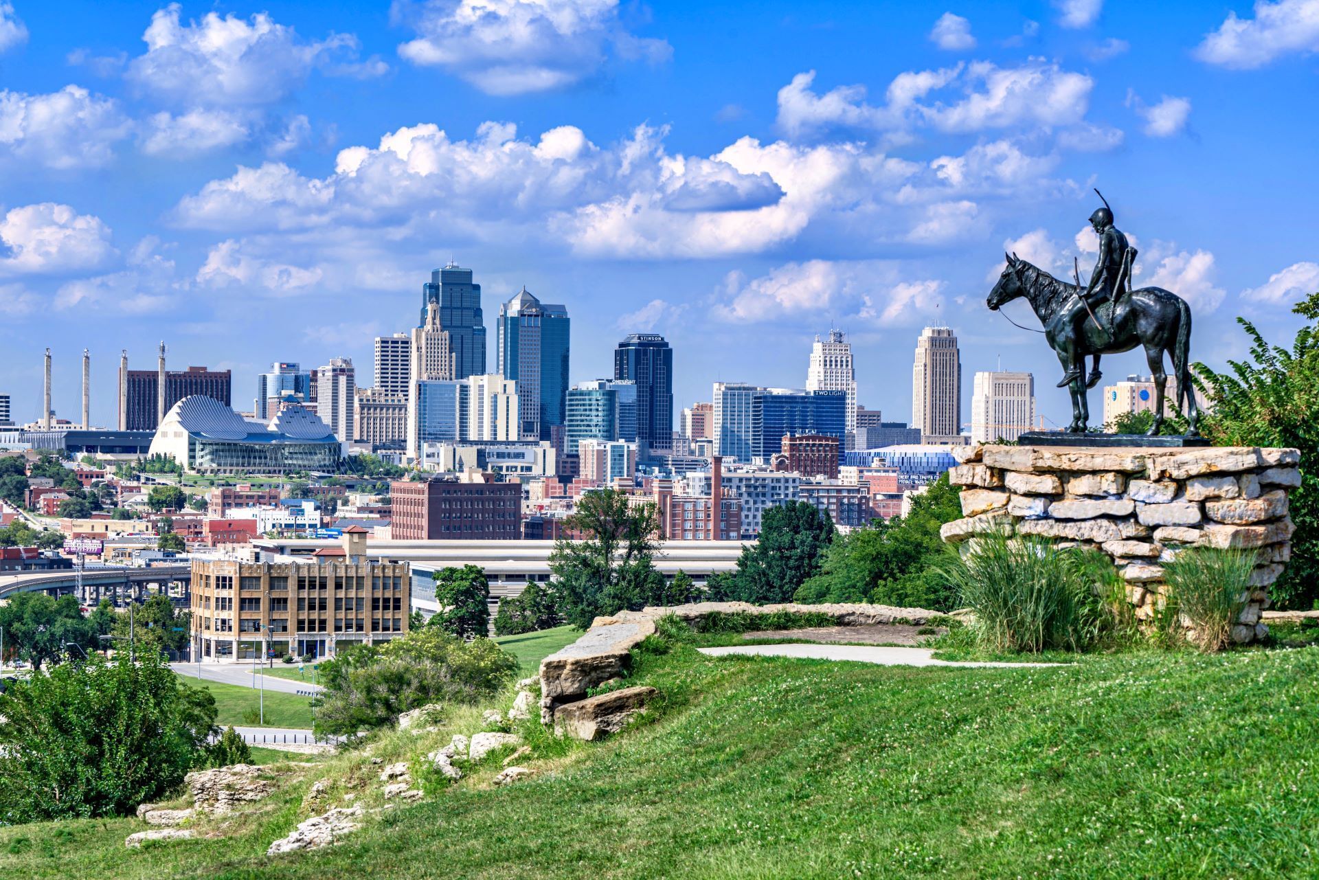 A statue of a man riding a horse with a city skyline in the background.