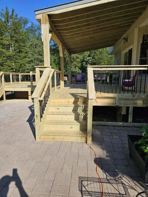Wooden deck with stairs, railings, and a covered porch extending from a beige house.