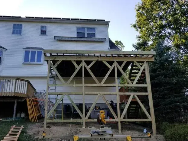 Construction of a two-story wooden deck attached to a white house; men are working on the framing.