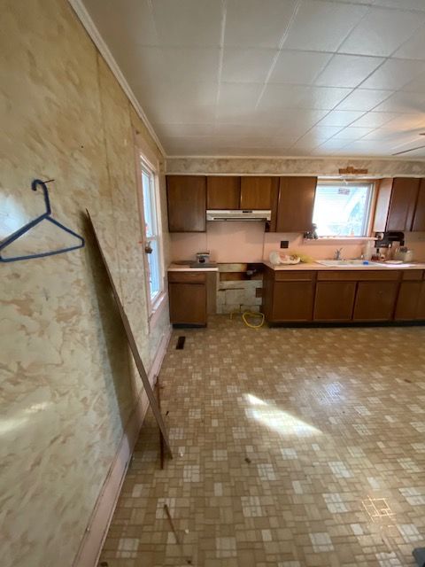 A drab kitchen with wood cabinets, peeling vinyl flooring, and a missing cabinet space.