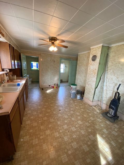 Kitchen with linoleum floor, cabinets, and doorway to other rooms. Light walls and a ceiling fan.