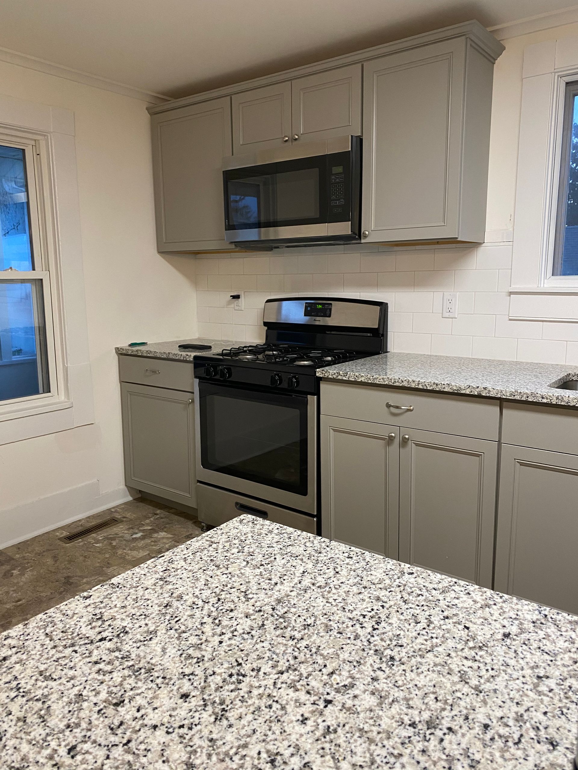 Gray kitchen cabinets with a granite countertop, stainless steel appliances, and white subway tile backsplash.