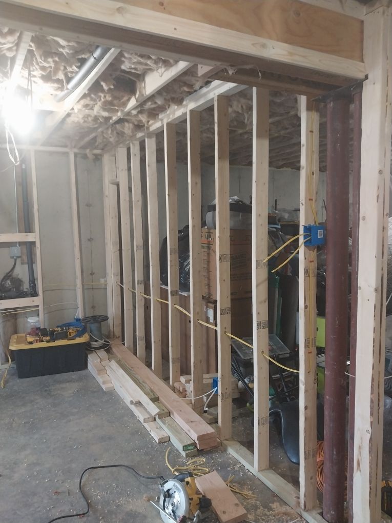 Interior of a room under construction with wooden studs, electrical wires, and tools scattered on the floor.