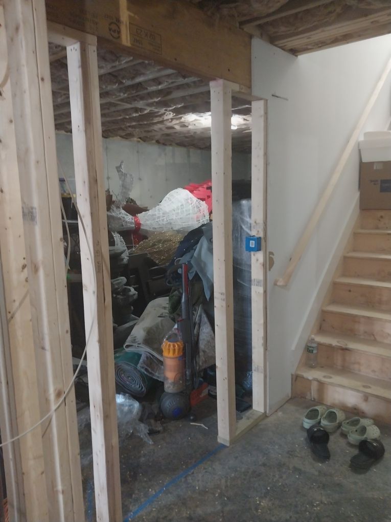 Unfinished basement doorway with staircase on the right, cluttered storage area in the background.
