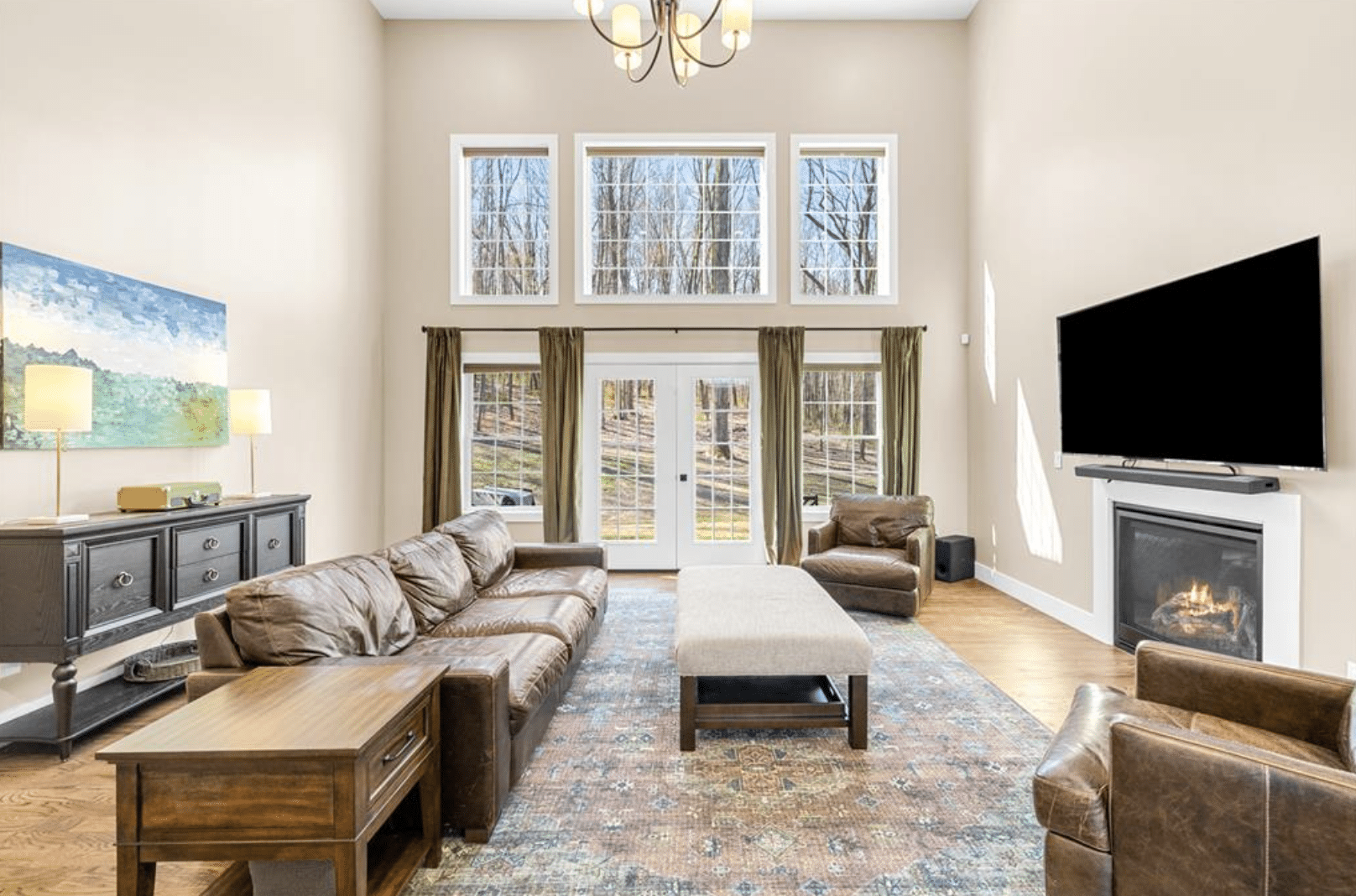A living room with tall windows, fireplace, and a brown leather sectional.