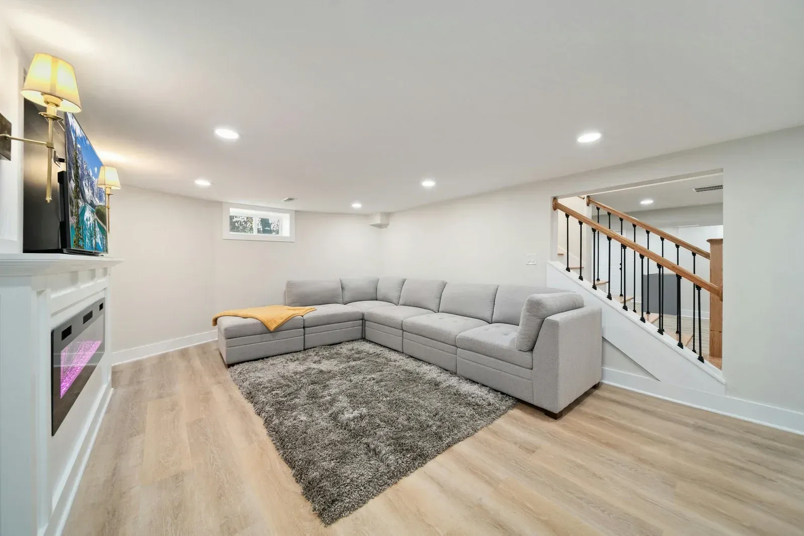 Cozy basement living space with gray sectional sofa, fireplace, rug, and staircase.