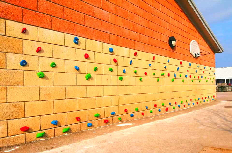 Climbing wall on brick building with colorful handholds.