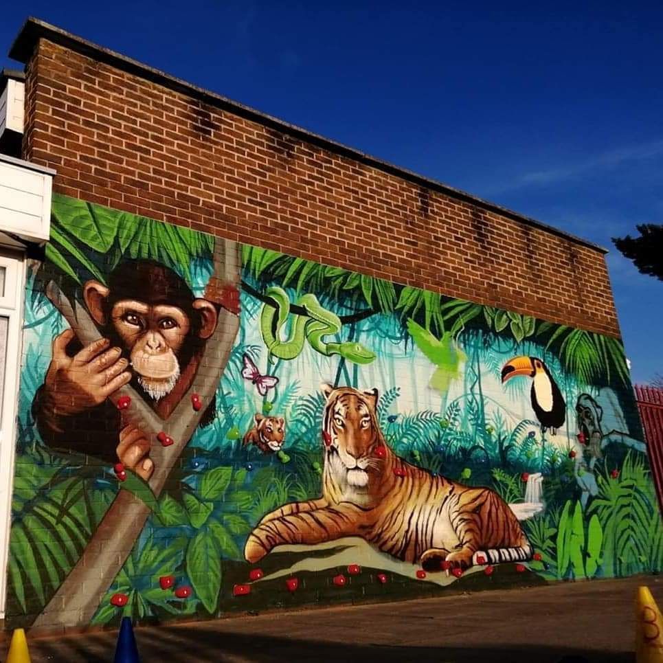 Jungle-themed mural on a brick wall: monkey, tiger, toucan, snake, butterfly, lush green foliage against a blue sky.