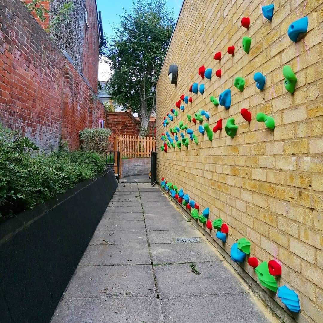 Narrow alley with a climbing wall on a brick wall. Holds are colorful.
