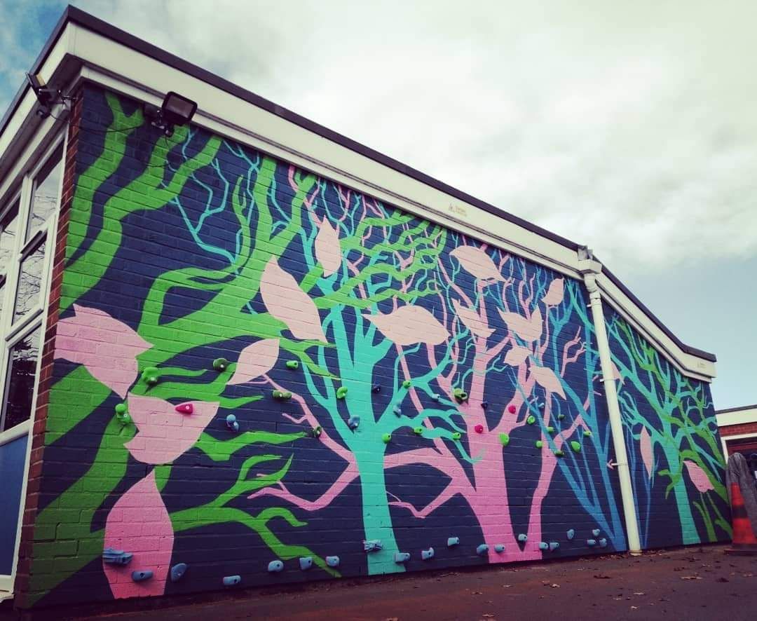 Mural of colorful trees painted on a brick building's exterior wall. Green, blue, and pink hues.