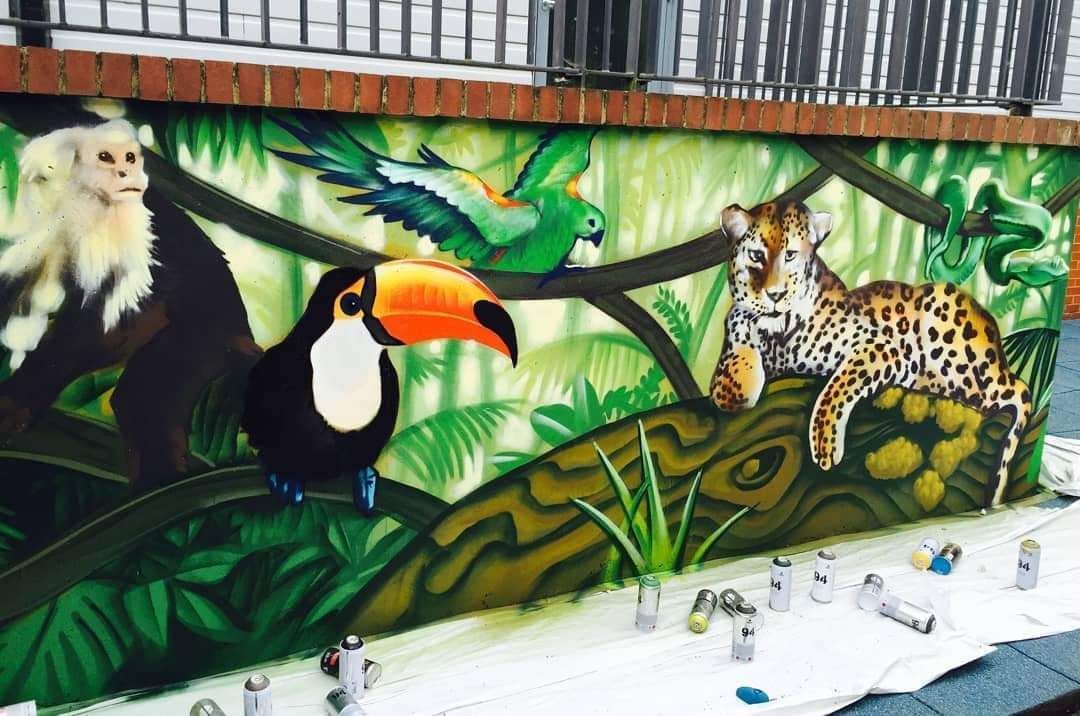 Mural of jungle animals: monkey, toucan, parrot, leopard on a green and brown background.