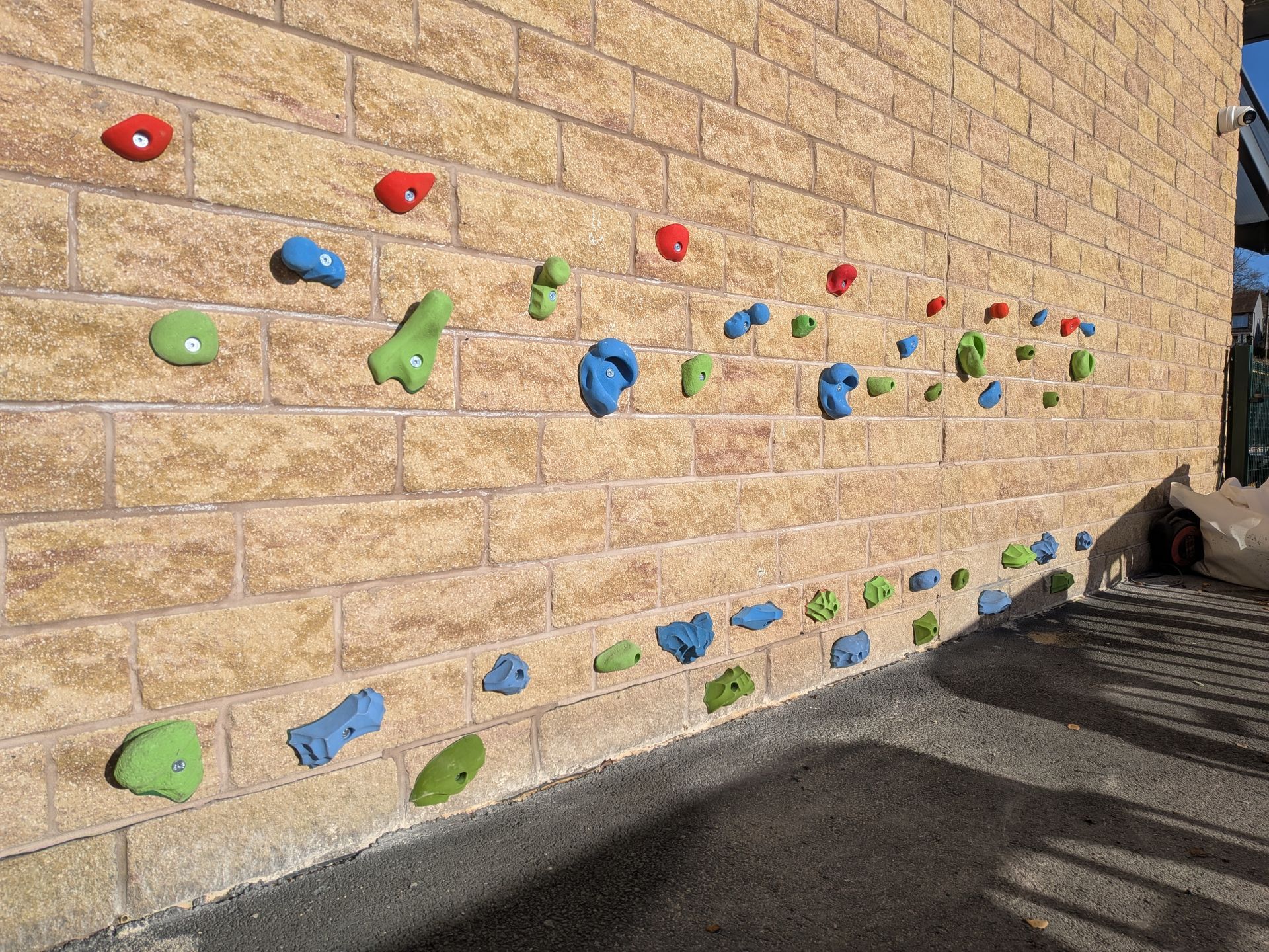 Climbing wall with colorful handholds on a brick wall. Sunlight casts shadows.