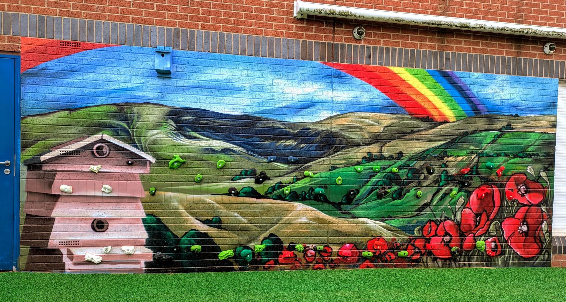Mural of rolling hills, rainbow, and poppies; painted on a wooden fence, with a beehive structure on the left.