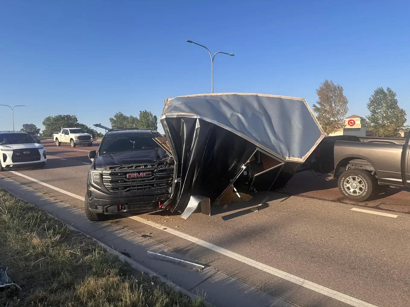 Black SUV and tan pickup truck involved in a collision with a damaged enclosed trailer on a road.