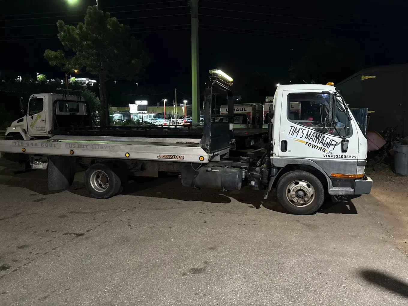 Tow truck parked at night, flatbed empty. White cab, black equipment.