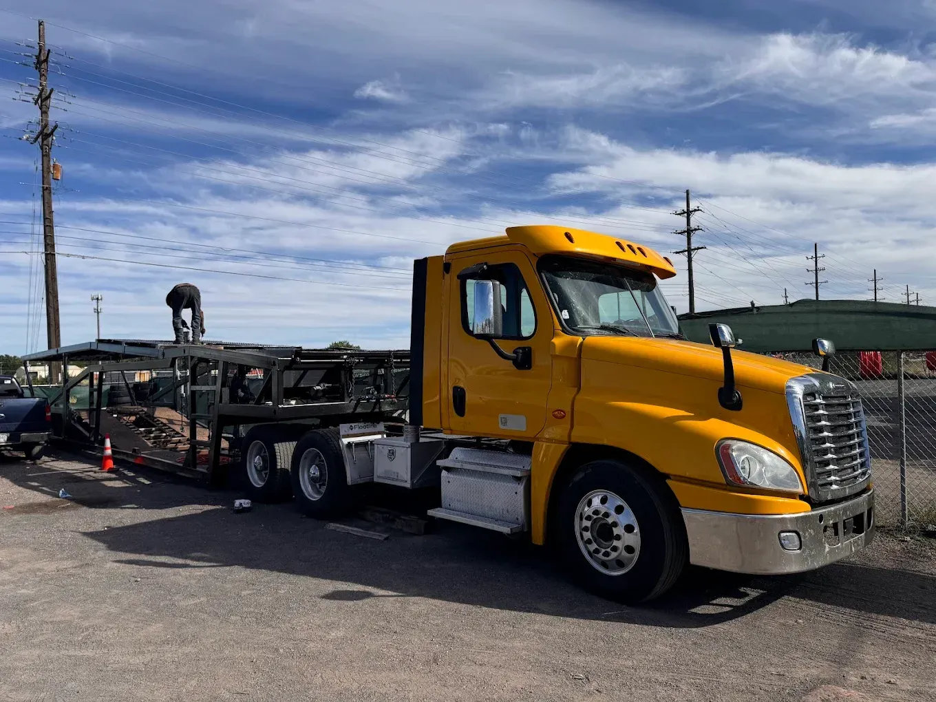Yellow semi-truck with car carrier. A person on the carrier. Cloudy sky.